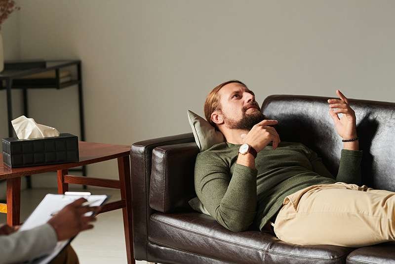 Man reclining on sofa during therapy session.