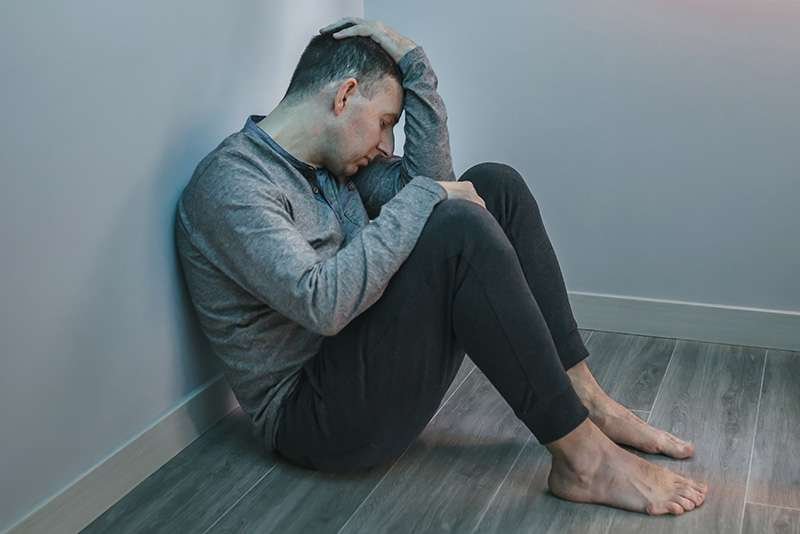 Man sitting on floor, looking distressed or upset.