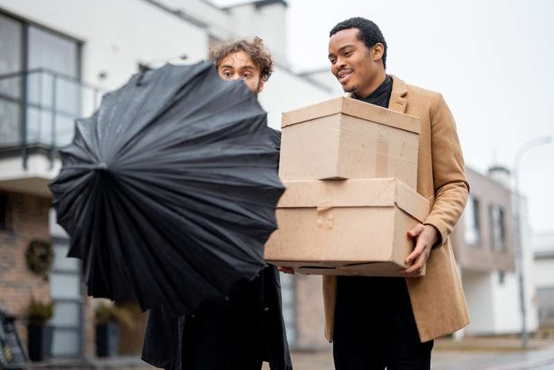 Men carrying boxes in windy weather with umbrella